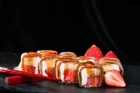 Fotografía profesional de un plato de sushi dulce decorado con rodajas de plátano, fresas y un toque de crema de avellanas.