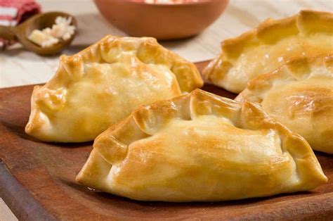 Fotografía gastronómica de empanadas artesanales con diversos repulgues y rellenos expuestas en una bandeja