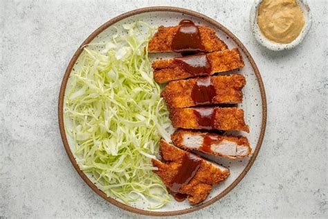 Fotografía profesional de un Tonkatsu servido con ensalada de col fresca y una montaña de arroz blanco al estilo tradicional.