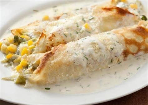 Fotografía de panqueques rellenos de pollo y choclo con salsa blanca.