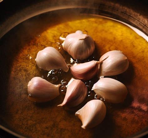 Dientes de ajo, romero y guindillas confitándose lentamente en aceite de oliva en una olla.