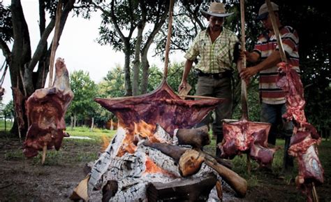 Varas con carne ensartada asándose lentamente alrededor de una hoguera