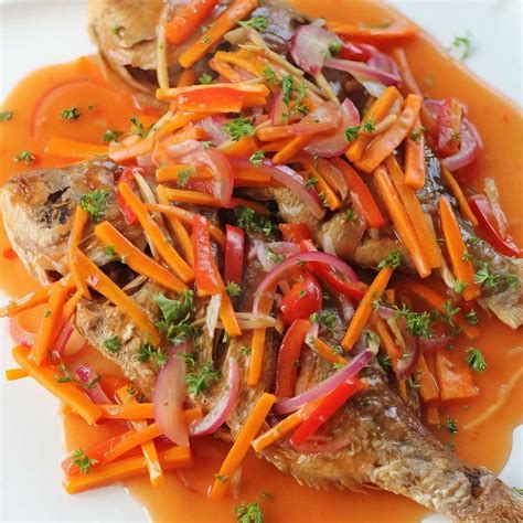 Fotografía de un plato terminado de pescado en escabeche servido con rodajas de zanahoria y cebolla, acompañado de guarniciones tradicionales como huevo duro o camote.