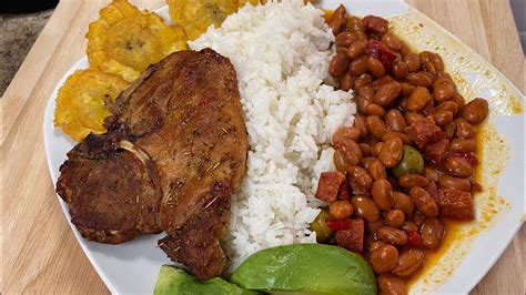 Plato servido de arroz con habichuelas rojas acompañado de una chuleta de cerdo dorada y vegetales frescos.