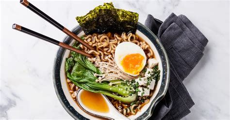 Un plato de ramen humeante con todos sus ingredientes y un par de palillos.