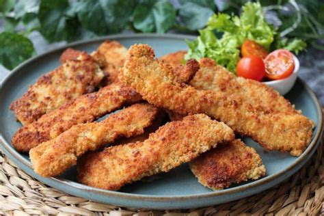Tiras de chicharrón de pollo crujientes y doradas, servidas con gajos de limón.