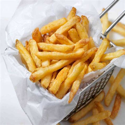 Patatas fritas doradas y crujientes en una cesta, escurriendo sobre papel de cocina