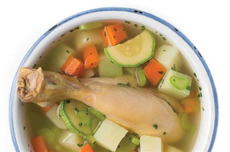 Un tazón humeante de caldo de pollo con verduras frescas