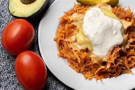 Plato de fideo seco servido con crema, queso y aguacate como presentación tradicional