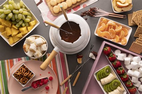 Mesa con una fondue de chocolate humeante y varios cuencos con frutas y dulces para mojar