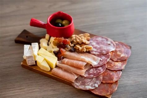 Fotografía profesional de una selección de carnes frías (jamón, salami y chorizo) dispuestas sobre una tabla de madera.
