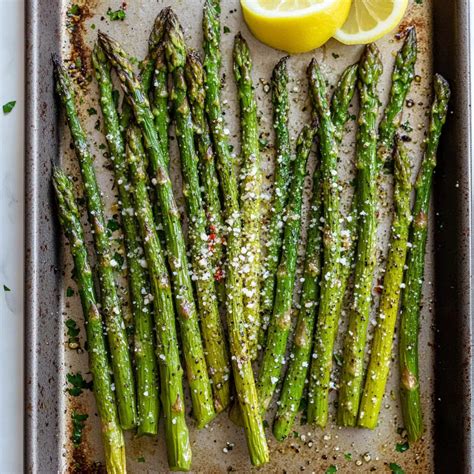 Imagen de una bandeja de horno con espárragos verdes recién horneados, dorados y crujientes, espolvoreados con queso y hierbas
