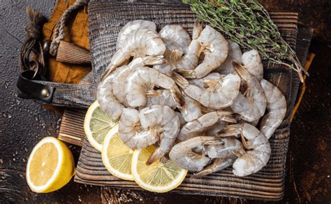 Ilustración de los ingredientes frescos necesarios para preparar camarones con limón, incluyendo camarones crudos, limones, chiles serranos, cebolla morada y pepino.