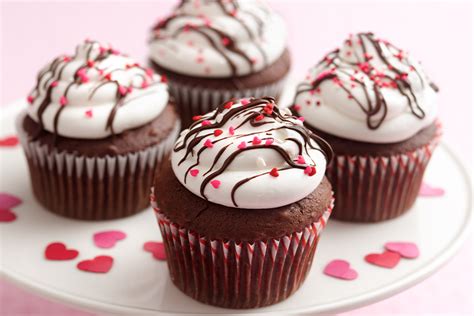 Variedad de cupcakes decorados creativamente para San Valentín, algunos con mensajes escritos y otros con figuras.