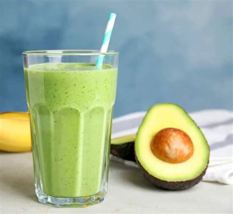 Fotografía de un smoothie de aguacate servido en un vaso decorado con pistachos y crema batida