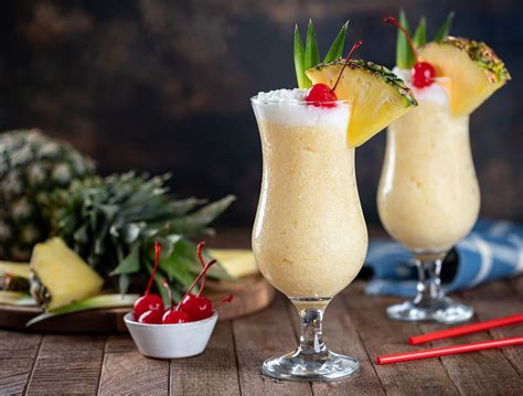 Foto profesional de un cóctel Piña Colada servido en una copa huracán con decoración de piña y cereza.