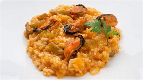 Imagen de un plato de arroz con mejillones bien presentado, decorado con mejillones enteros en su concha y perejil picado.