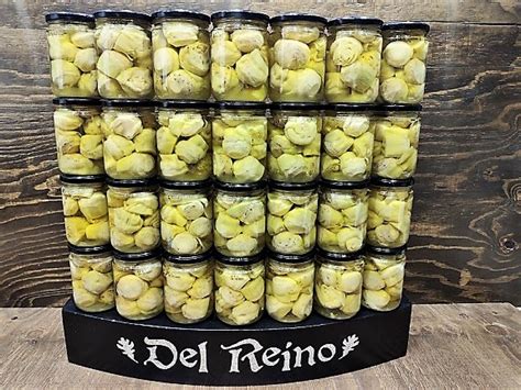 Tarro de conservas de alcachofas enteras junto a unas alcachofas frescas.