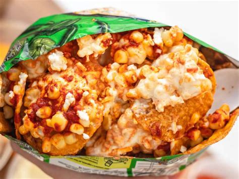 Fotografía cenital de un plato de Tostitos servidos con una mezcla de elote, crema y salsas picantes.
