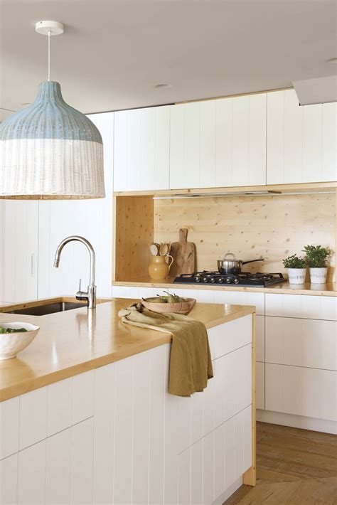 Cocina moderna con muebles blancos y encimera de madera tratada.