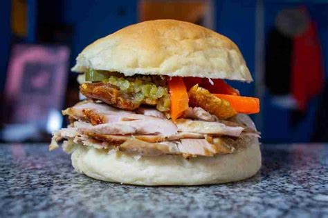 Primer plano de los ingredientes del sándwich de chola: carne de cerdo deshebrada, escabeche, cuerito crujiente y rodajas de tomate.