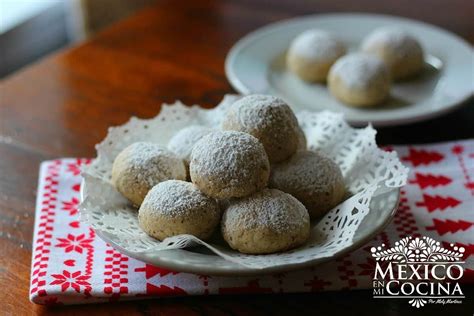 Foto de bolitas de galletas caseras decoradas con azúcar glas y trocitos de nuez, presentadas en una bandeja.