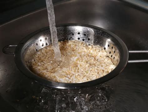 Arroz japonés en un colador siendo lavado, el agua se vuelve transparente