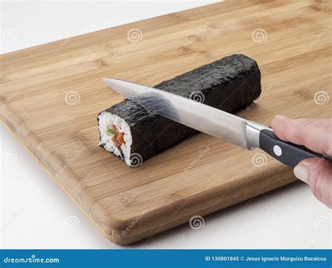 Cuchillo de sushi afilado y humedecido cortando un rollo de sushi en una tabla