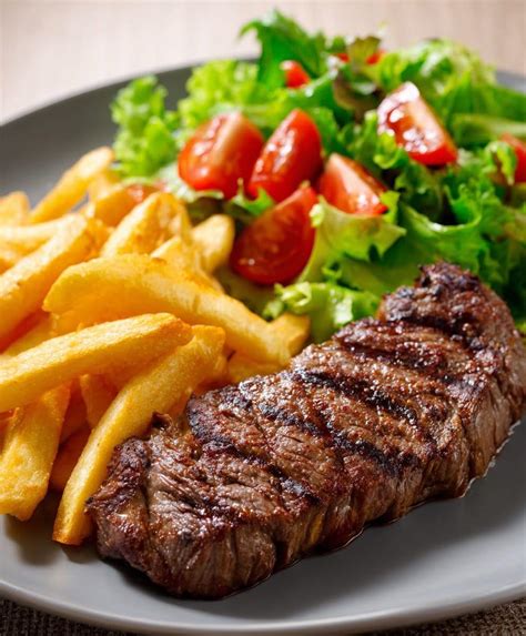 Plato de chuletas a la parrilla servidas con papas doradas y una ensalada fresca. Una salsa chimichurri en un recipiente pequeño.