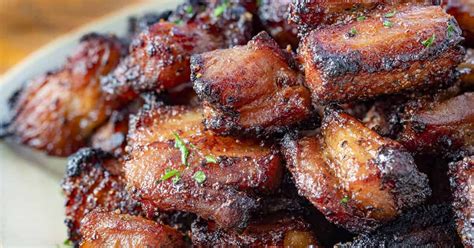 Fotografía de papas dorándose en una plancha junto a trozos de panceta y hierbas frescas