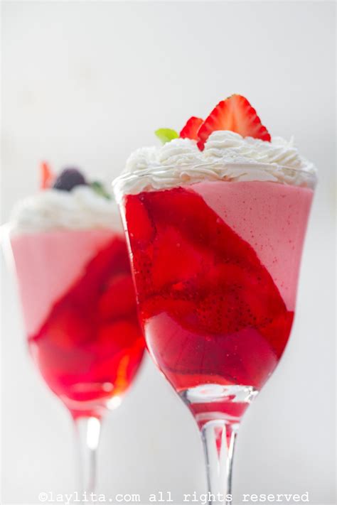 Foto de copas elegantes servidas con capas de gelatina roja y crema blanca decoradas con frutas frescas coloridas