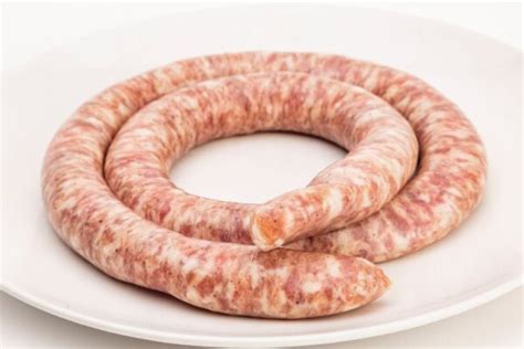 Primer plano de una longaniza blanca (Bratwurst) cocinándose en la parrilla, mostrando su textura dorada.