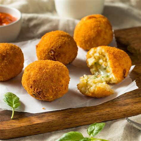 Plato de croquetas de arroz sin pan rallado, doradas y humeantes, con un aderezo al lado.
