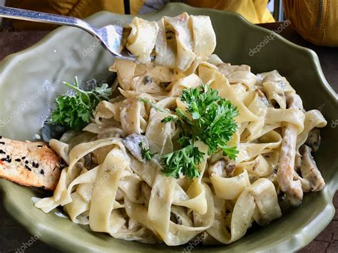 Plato de fettuccine Alfredo servido con perejil fresco picado.