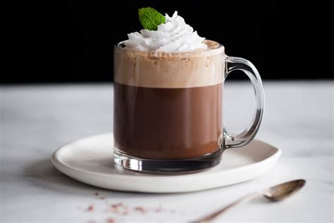 Fotografía de una taza humeante de café moca con menta caliente, decorada con nata y canela.
