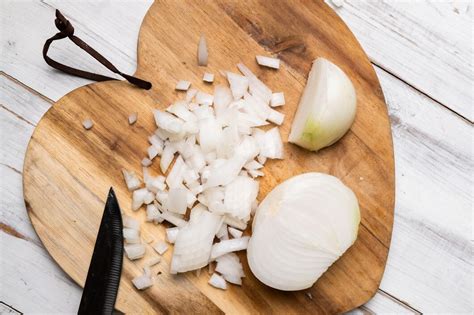 Cebolla blanca cortada y entera en una tabla de cortar, resaltando su pulpa blanca y firme.