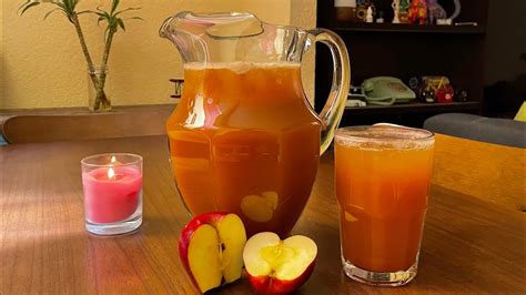 Una jarra de agua fresca de manzana con canela junto a una manzana y una rama de canela.