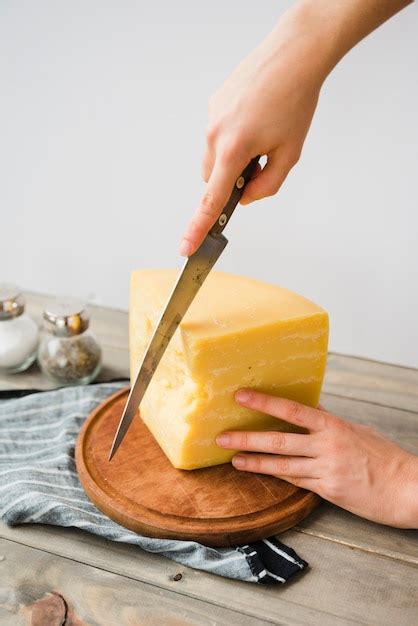 Persona cortando queso con un cuchillo limpio sobre una tabla de cortar higiénica