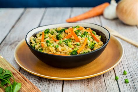 Plato de arroz frito con huevo revuelto, trozos de verduras coloridas (zanahoria, brócoli, guisantes) y cebolla cambray picada.