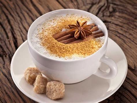 Un café latte con espuma y un toque de vainilla, rodeado de granos de café y vainas de vainilla