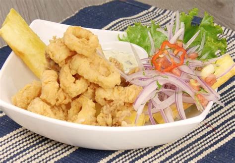Plato de chicharrón de calamar frito, crujiente y dorado, con gajos de limón y salsa criolla.