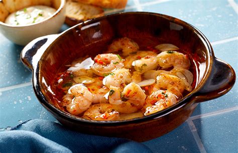 Imagen de camarones al pil pil servidos en cazuelitas individuales de barro, acompañados de pan rústico