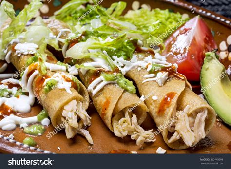 Foto de rollos de tacos fritos de pollo servidos con salsa y guarniciones