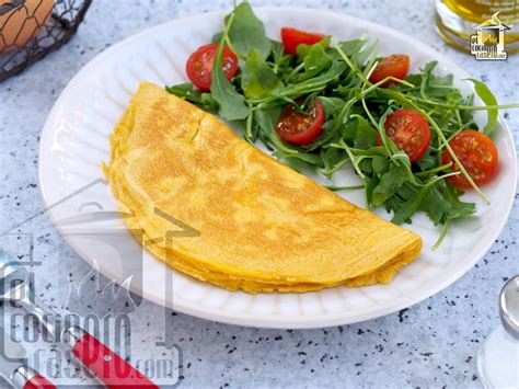 Dos tortillas distintas en una tabla de cortar, una de ellas la tortilla francesa de huevos batidos plegada y la otra una tortilla de maíz para tacos.