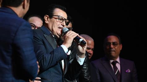 Foto de Ismael Miranda en concierto, con un micrófono y su orquesta al fondo