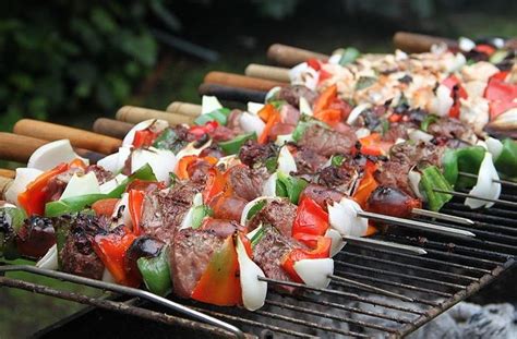 Fotografía de anticuchos de vacuno listos para ser cocinados en la parrilla, intercalando carne, chorizo, cebolla y pimientos.