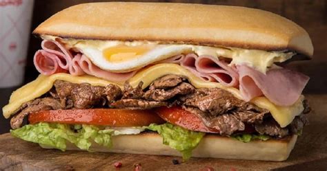 Fotografía de un sándwich de lomito con queso y vegetales en un ambiente de bar