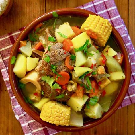 Fotografía de un plato servido de carne a la olla al vino tinto, acompañado de puré de papas y una ramita de perejil.