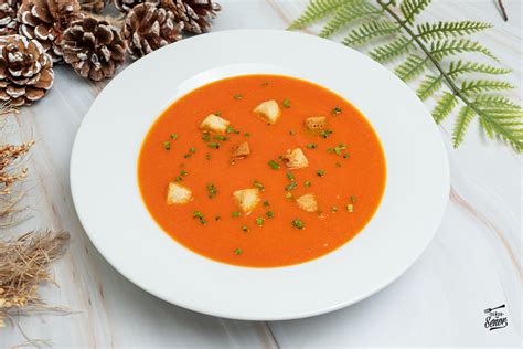 Sopa de tomate casera en un tazón con guarniciones y un trozo de pan