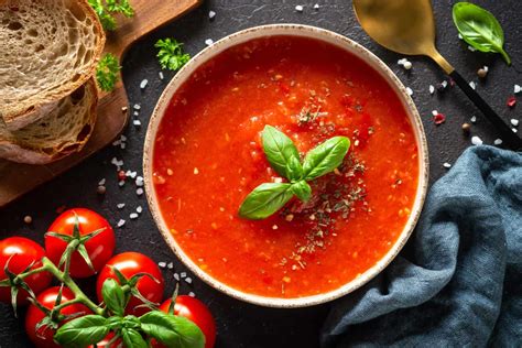Sopa de tomate servida en un plato hondo con guarnición de hojas de albahaca y crema